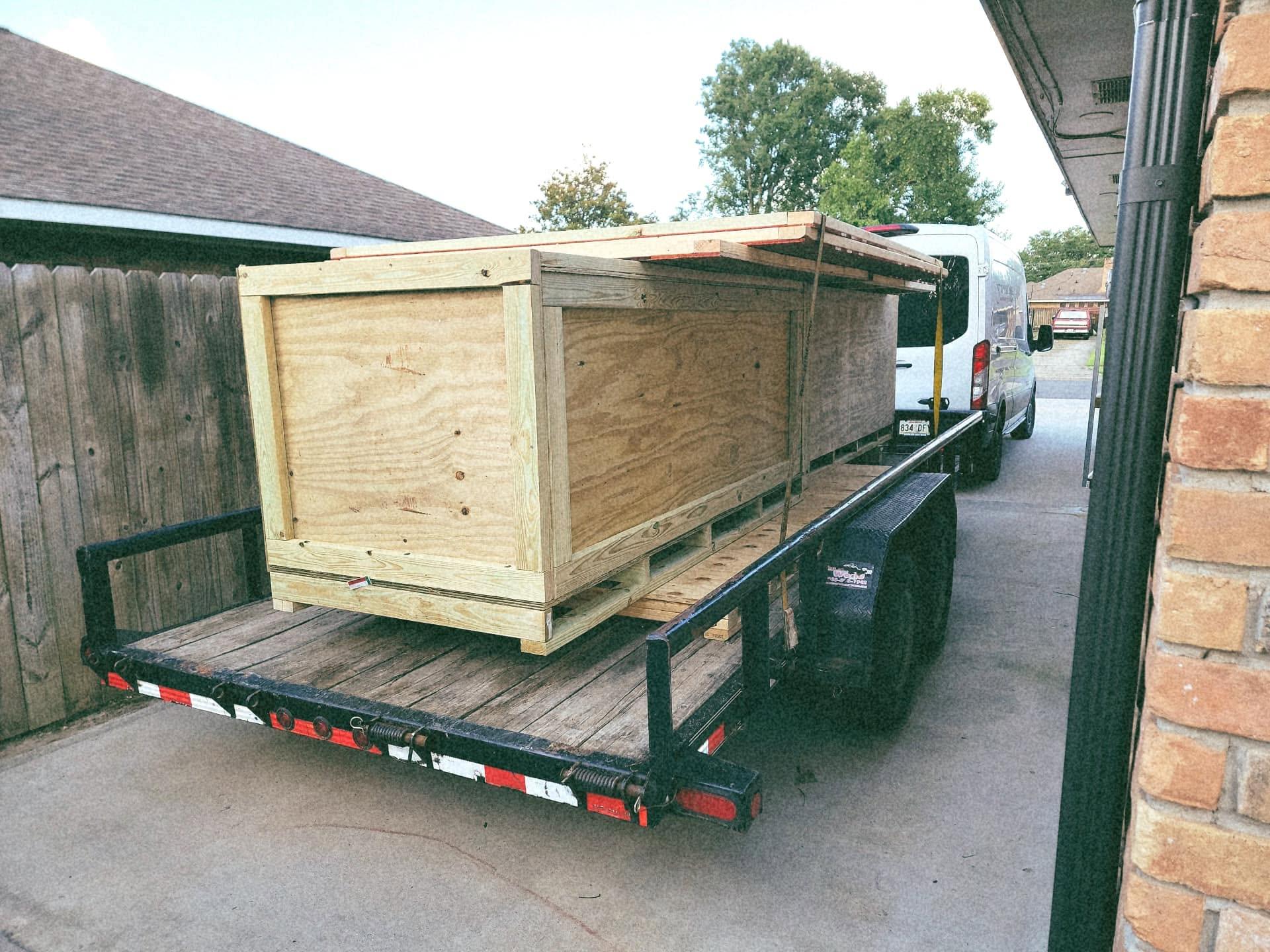 A large plywood crate strapped to a flatbed trailer, with the company van ahead of it