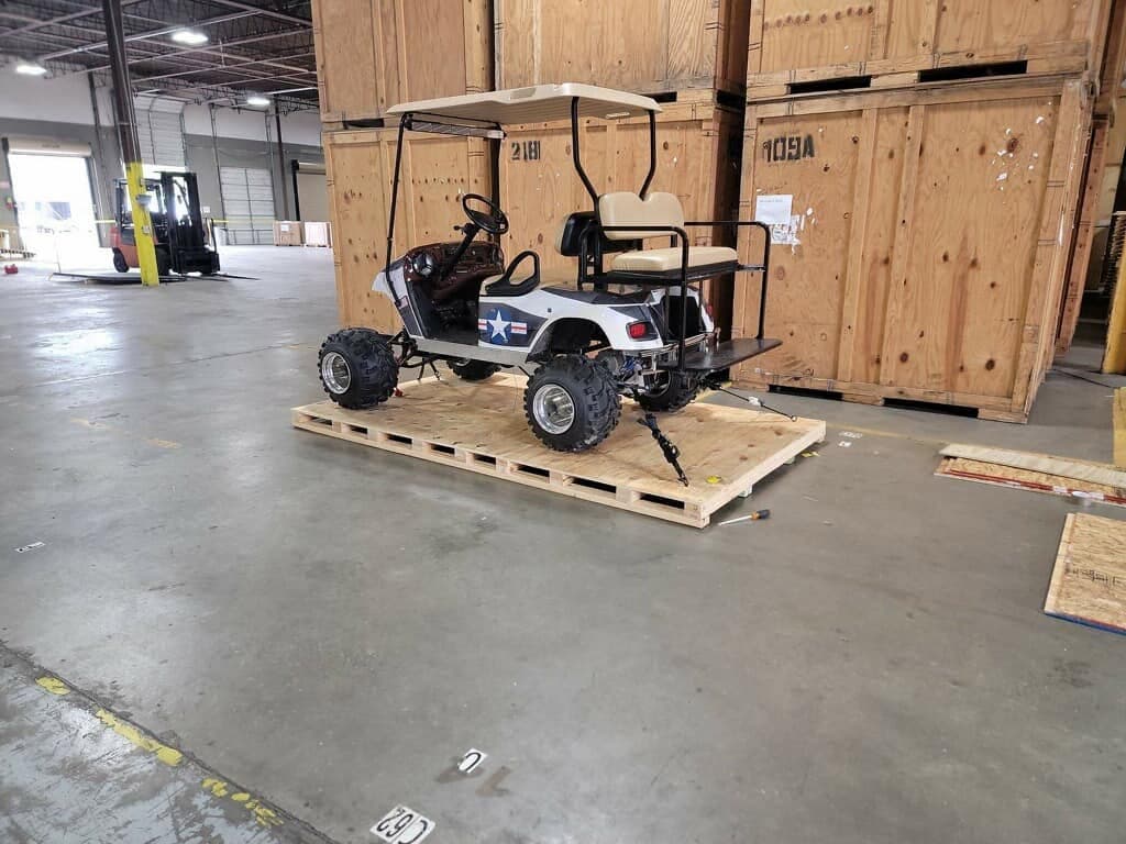 A golf cart strapped to a skid in a warehouse, ready to be crated