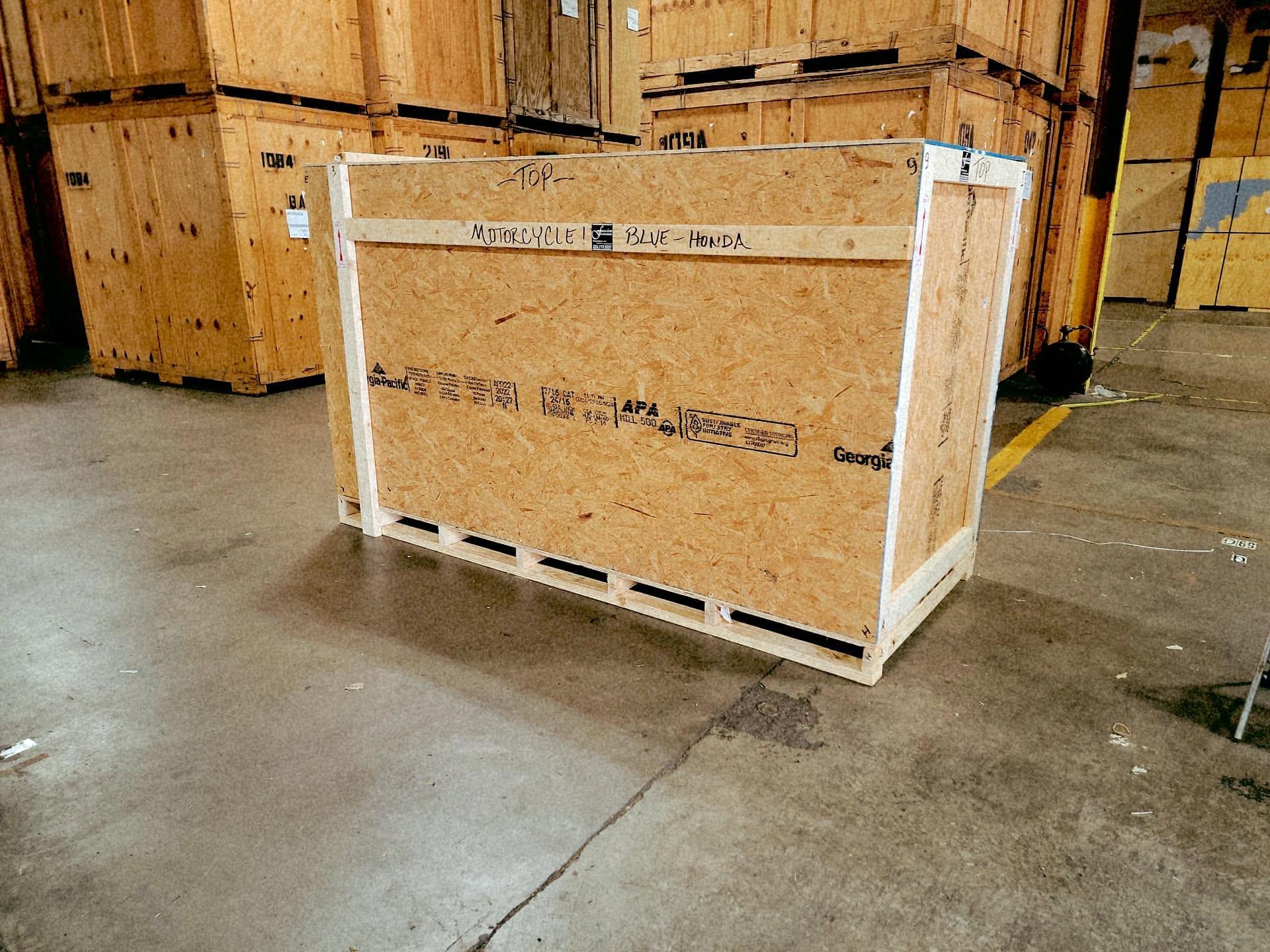 A custom crate for a motorcycle in a warehouse, with stacked crates behind it